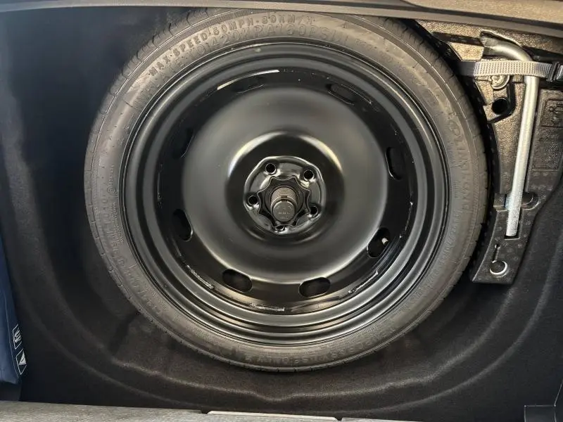Roue de secours noire en gros plan dans le coffre d'une Volkswagen Golf 2024 gris dauphin métallisée.