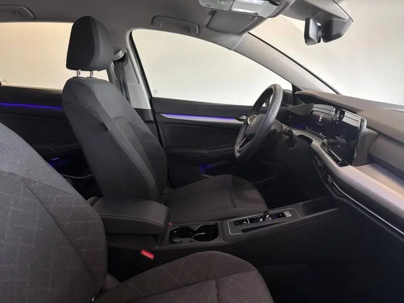 Vue intérieure côté conducteur de la Volkswagen Golf 2024, sièges tissu Maze noir et éclairage d'ambiance bleu subtil
