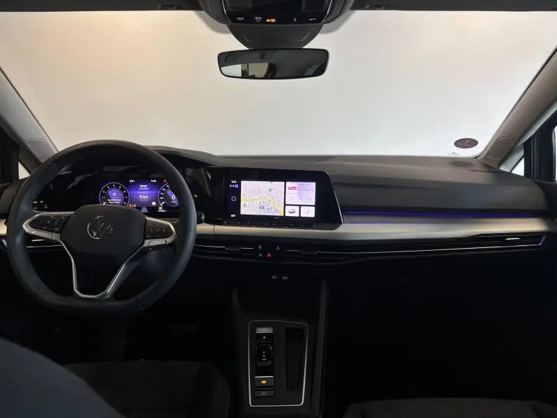 Tableau de bord et volant cuir multifonction d'une Volkswagen Golf 2024, avec écran tactile et éclairage d'ambiance bleu.