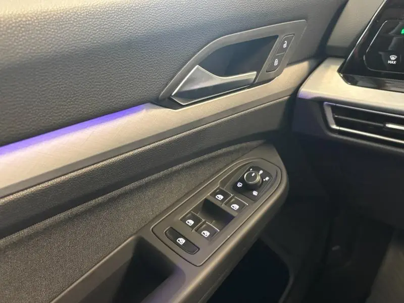 Détail de la porte côté conducteur de la Volkswagen Golf 2024 gris dauphin, avec commandes de vitres et éclairage d'ambiance violet.
