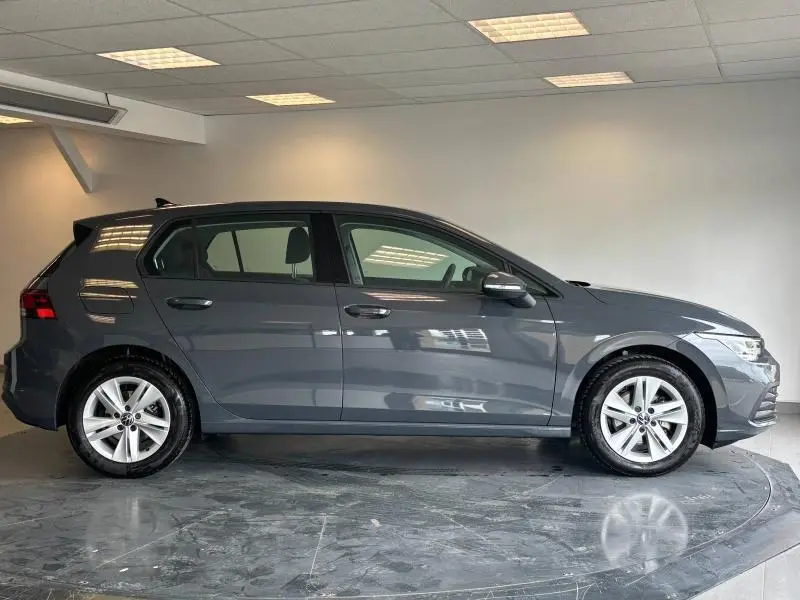 Profil côté gauche d'une Volkswagen Golf 2024 gris dauphin métallisé avec jantes alu dans un showroom lumineux.