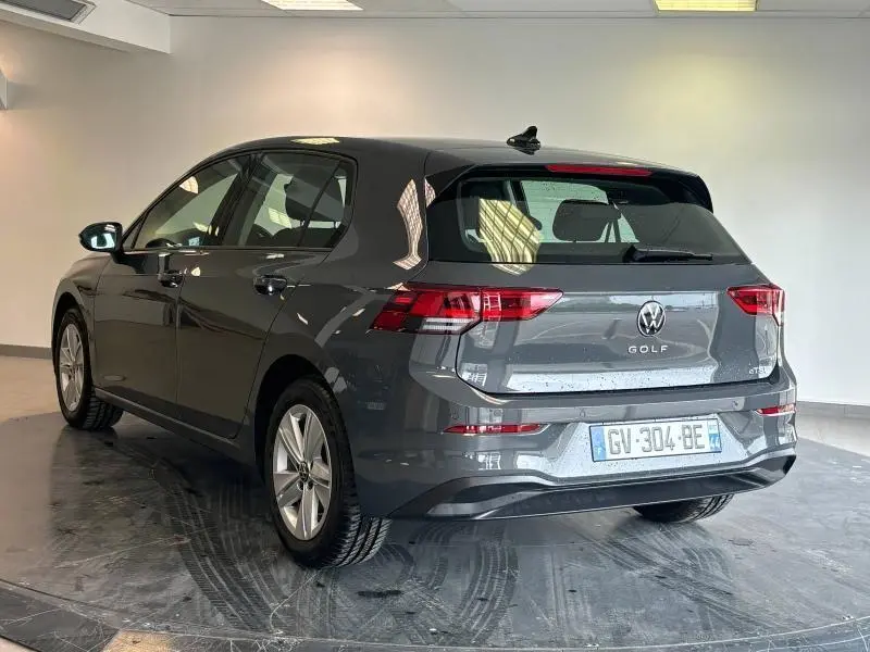 Volkswagen Golf 2024 gris dauphin métallisé vue 3/4 arrière droit en intérieur avec feux LED et jantes alu.