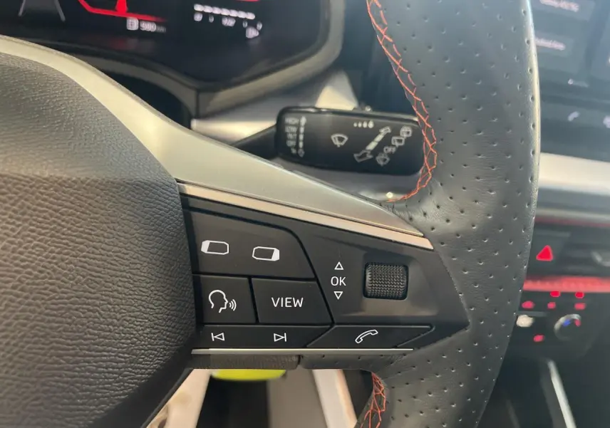 Gros plan sur le volant sport cuir noir perforé avec surpiqûres rouges du SEAT Arona 2024, boutons multifonctions visibles.