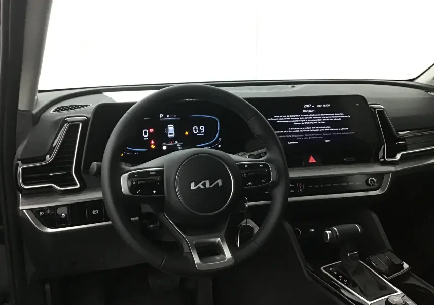 Vue intérieure du tableau de bord du Kia Sportage 2025 noir, avec volant cuir et écran digital 12,3 pouces.