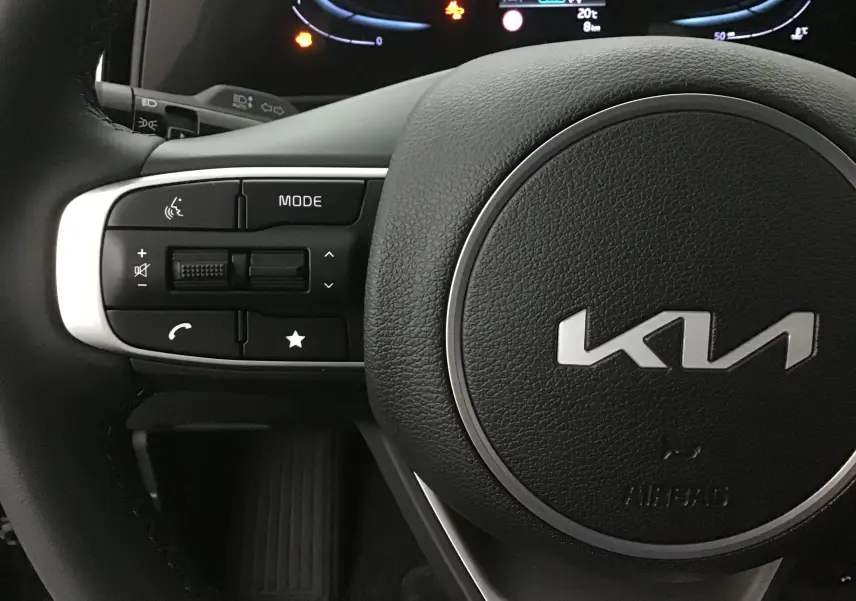 Gros plan sur le volant noir du Kia Sportage 2025 avec commandes intégrées et logo KIA au centre.