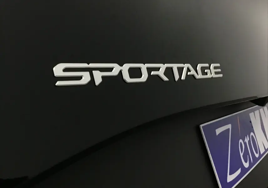 Gros plan sur l’inscription SPORTAGE en lettres argentées sur la carrosserie noire brillante d’un Kia 2025.