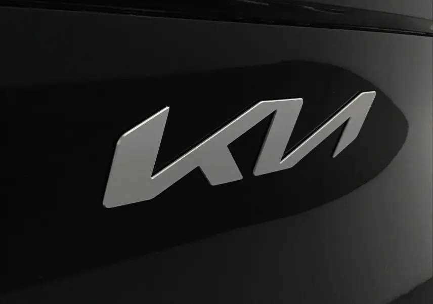Gros plan sur le logo KIA argenté sur la carrosserie noire brillante du SUV Sportage 2025.