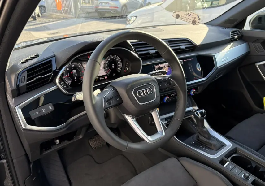 Intérieur de l'Audi Q3 Sportback 2025 vu côté conducteur, volant cuir, tableau de bord numérique et console centrale moderne.