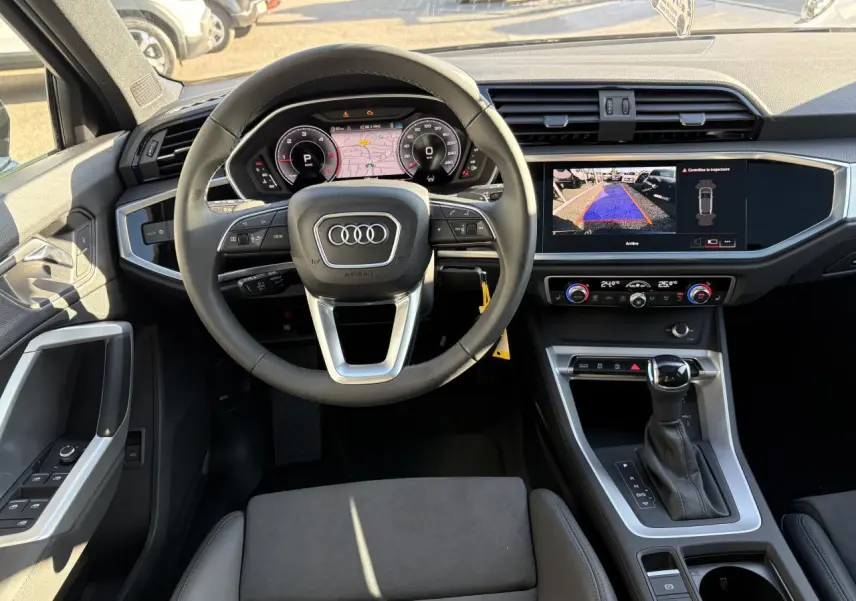 Vue intérieure avant de l'Audi Q3 Sportback 2025, volant cuir, tableau de bord numérique et écran central affichant la caméra de recul.