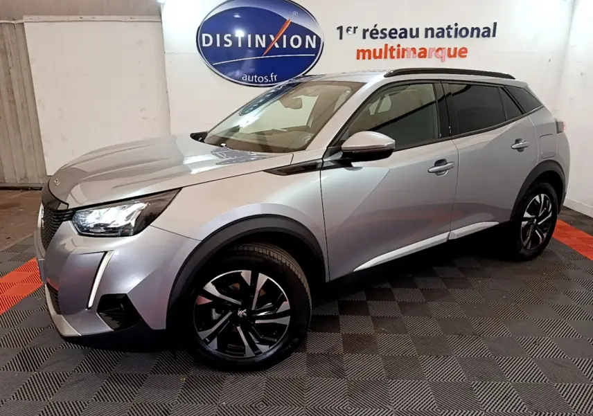 Peugeot 2008 gris clair en 3/4 avant droit, avec jantes noires et toit noir, dans un showroom intérieur.