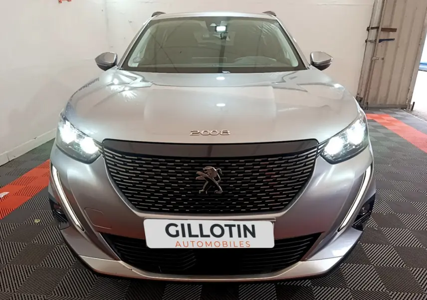 Vue frontale d'un Peugeot 2008 gris clair avec phares allumés et calandre noire distinctive en intérieur showroom.