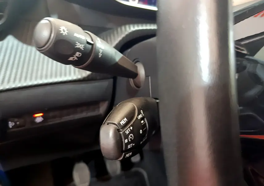 Gros plan sur les commandes au volant noir du Peugeot 2008 gris clair, mettant en valeur les fonctions de régulateur et éclairage.