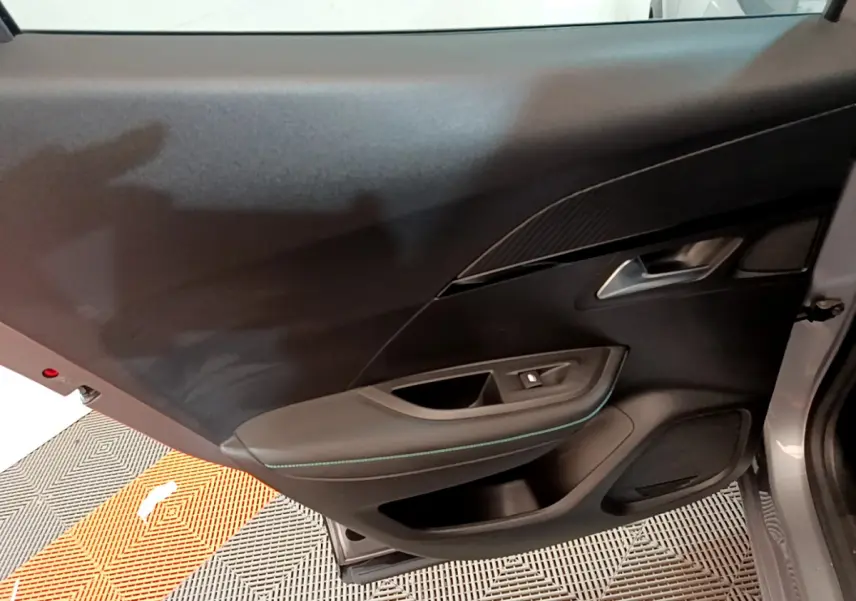 Vue intérieure de la porte côté gauche du Peugeot 2008 gris clair, avec garniture noire et surpiqûres bleues.