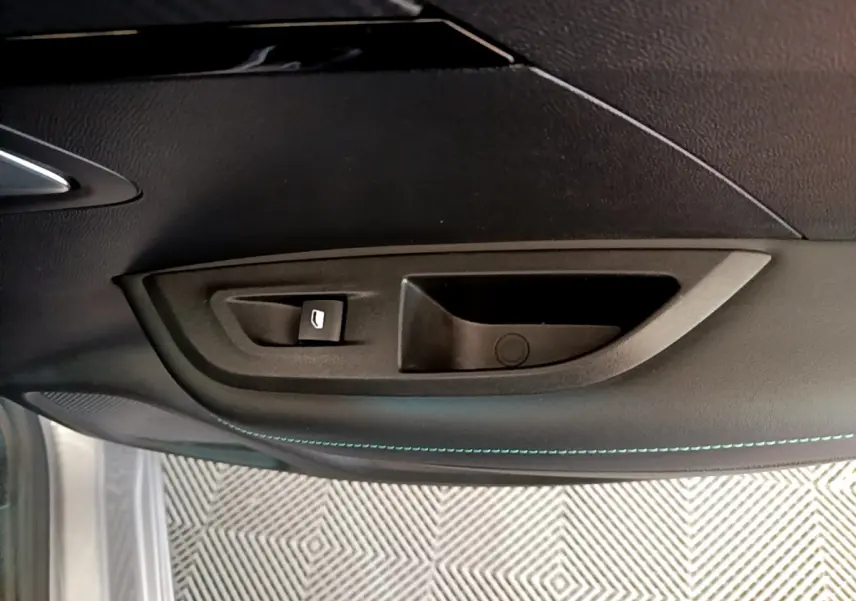 Poignée intérieure de porte côté gauche du Peugeot 2008 gris clair, avec bouton de commande de vitre et surpiqûres bleues.