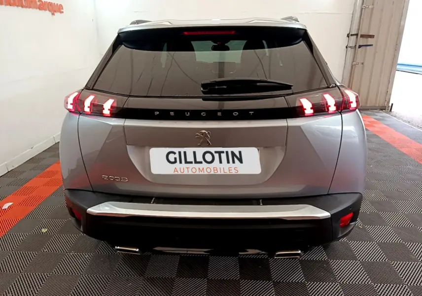 Vue arrière d'un Peugeot 2008 gris clair 2021 avec feux LED allumés dans un garage showroom.