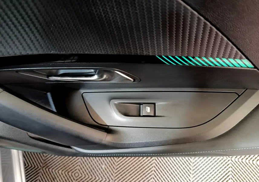 Détail de la porte côté gauche de la Peugeot 2008 gris clair, avec bouton de commande de vitre et insert décoratif vert.