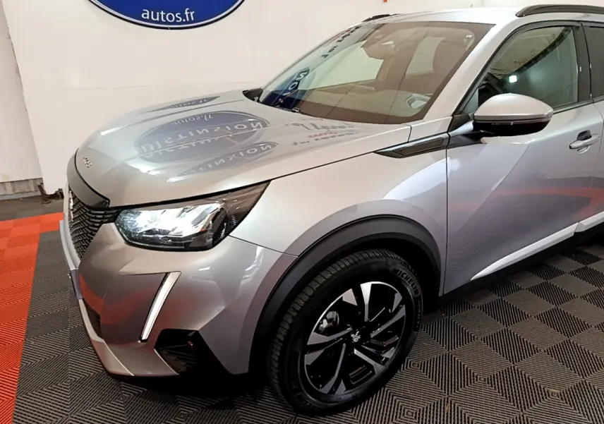 Peugeot 2008 gris clair vue 3/4 avant droit, avec phares LED et jantes noires distinctives.