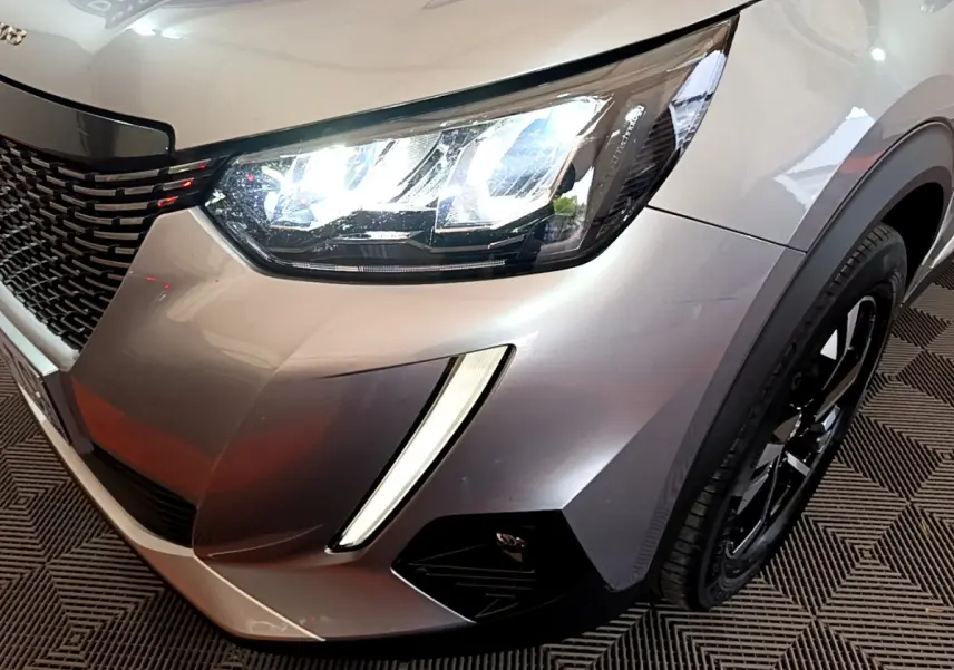 Gros plan sur l'avant droit gris clair du Peugeot 2008 avec ses phares LED allumés et la calandre noire.
