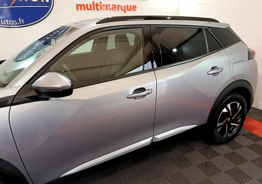 Profil côté gauche du Peugeot 2008 gris clair avec vitres teintées et jantes noires à motifs rouges.