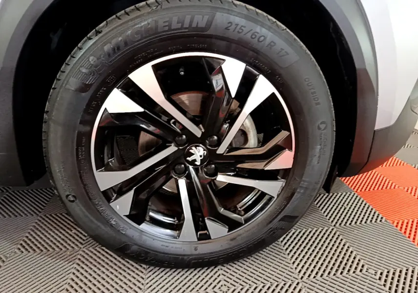 Gros plan sur la roue avant droite du Peugeot 2008 gris clair, mettant en valeur la jante alliage noire et argentée au design moderne.