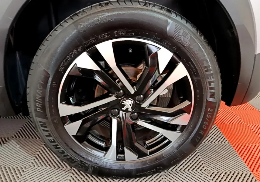 Gros plan sur la jante noire et argentée avec logo Peugeot d'un Peugeot 2008 gris clair, pneu Michelin visible.