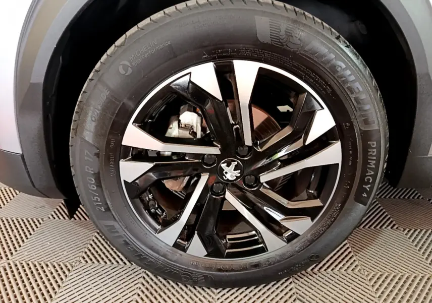Gros plan sur la roue avant gauche du Peugeot 2008 gris clair, avec jante alliage noire et argentée au design moderne.
