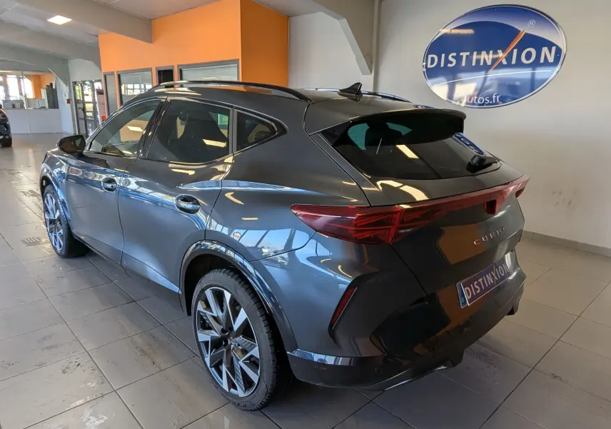 Vue 3/4 arrière droite du CUPRA Formentor gris magnétique métallisé, avec jantes alliage et vitres teintées en intérieur showroom.