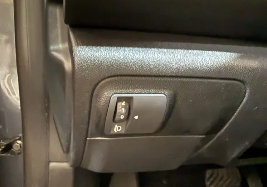 Détail du réglage des phares sur le tableau de bord noir de la Renault Mégane gris foncé, vue côté conducteur.
