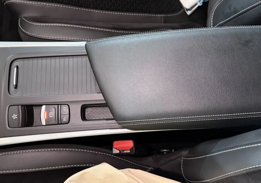 Gros plan sur la console centrale et l'accoudoir en cuir noir avec surpiqûres blanches d'une Renault Mégane gris foncé.