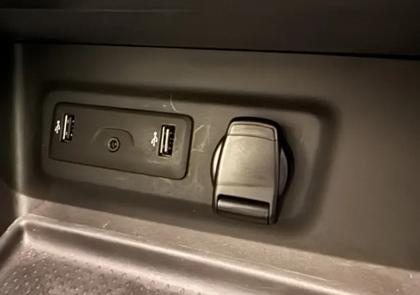 Prise USB double et prise 12V noire en gros plan dans le compartiment intérieur d'une Renault Mégane gris foncé.
