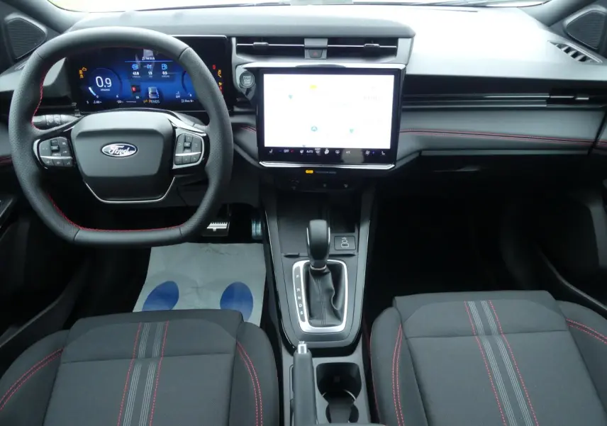 Vue intérieure frontale du Ford Puma 2025, tableau de bord noir avec surpiqûres rouges et écran tactile central lumineux.