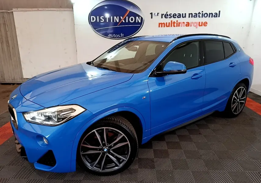 BMW X2 sDrive20i M Sport bleu en vue 3/4 avant droit, avec jantes sport et vitres teintées, intérieur beige visible.