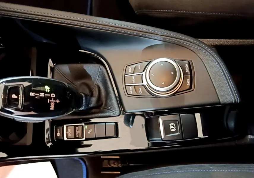 Gros plan sur la console centrale noire brillante du BMW X2 bleu, avec levier de vitesses automatique et molette de contrôle.