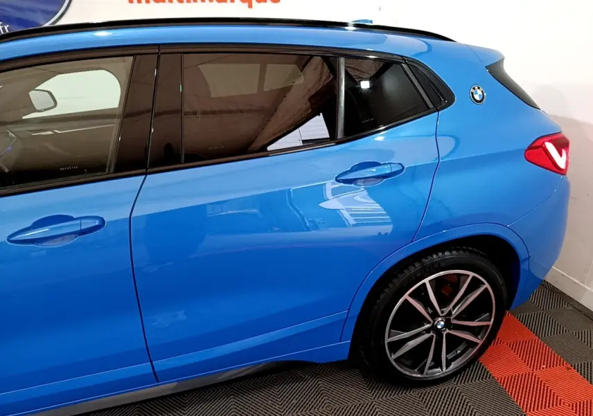 Vue latérale droite d'un BMW X2 sDrive20i M Sport bleu avec jantes alliage et logo BMW sur l'aile arrière.
