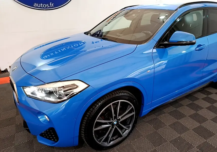 BMW X2 sDrive20i M Sport bleu en 3/4 avant droit, avec jantes alliage et phares LED visibles.