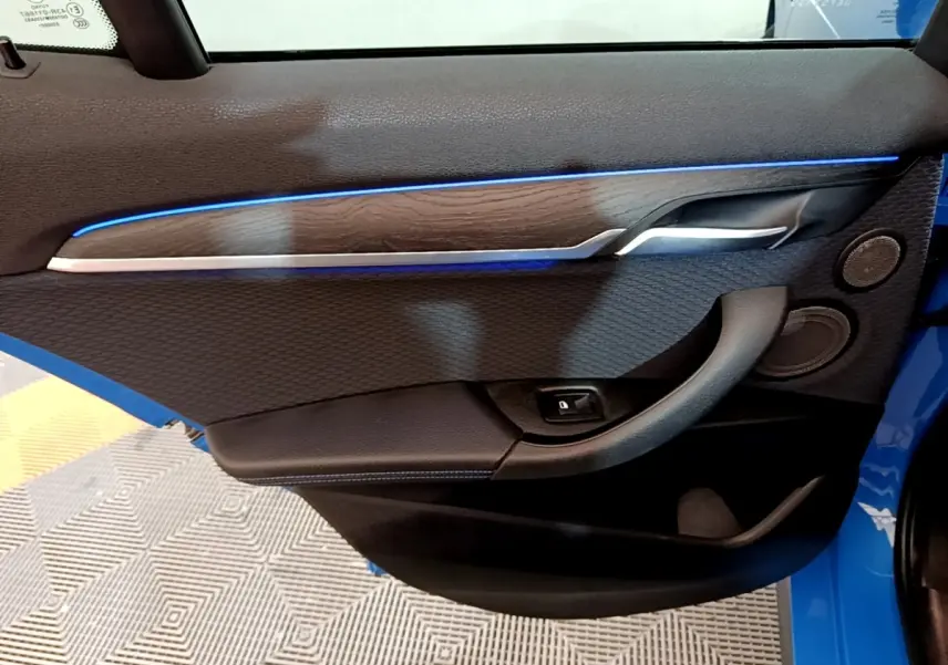 Gros plan sur la porte intérieure côté gauche du BMW X2 bleu, avec éclairage d’ambiance bleu et garniture bois.