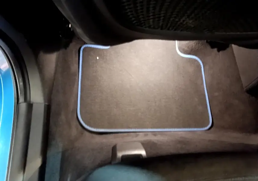 Vue intérieure du plancher côté passager arrière d'une BMW X2 bleu, avec tapis noir bordé de bleu.