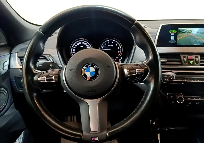 Vue intérieure centrée sur le volant cuir noir BMW M Sport avec tableau de bord et écran de caméra de recul.