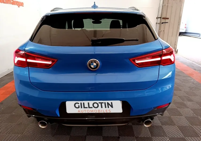 Vue arrière d’un BMW X2 sDrive20i M Sport bleu avec feux LED allumés et double sortie d’échappement chromée.