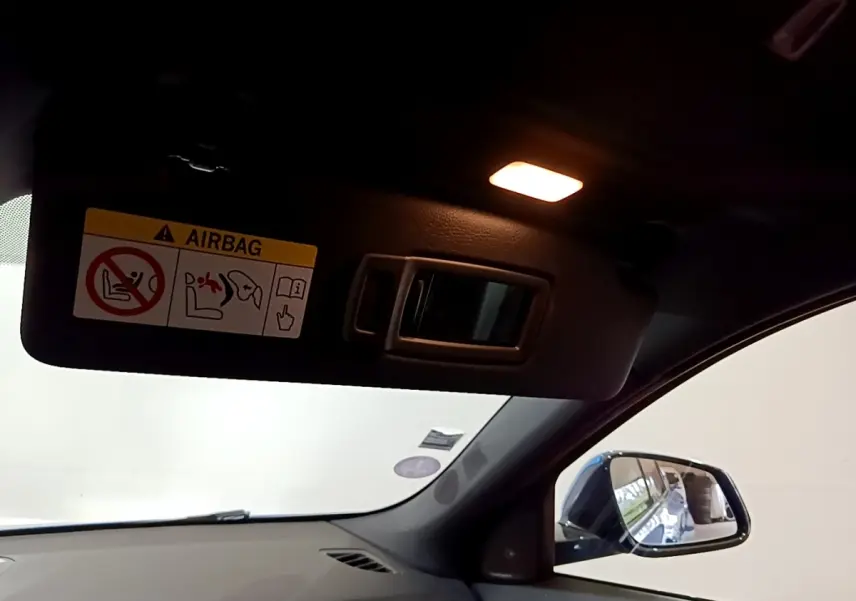Détail intérieur du pare-soleil côté conducteur avec miroir éclairé et rétroviseur extérieur bleu visible.