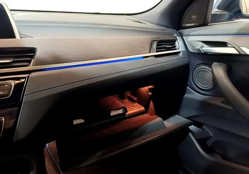 Intérieur côté passager du BMW X2 bleu, tableau de bord avec éclairage d'ambiance bleu et boîte à gants ouverte.