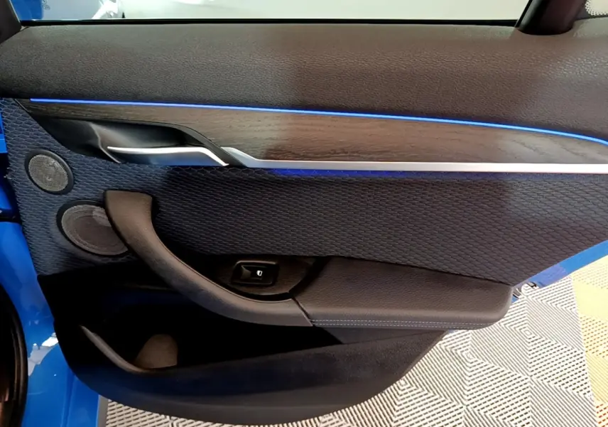 Vue rapprochée de la porte avant gauche d’un BMW X2 bleu, avec éclairage d’ambiance bleu et garniture noire texturée.