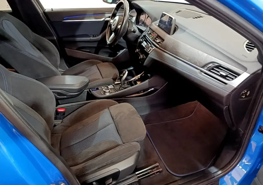 Vue intérieure côté passager avant d'une BMW X2 sDrive20i M Sport bleu, avec sièges en alcantara et tableau de bord moderne.