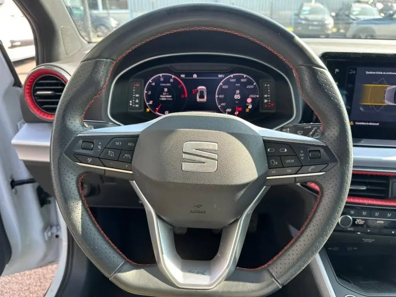 Vue rapprochée du volant perforé avec surpiqûres rouges du SEAT Arona 2025, tableau de bord numérique en arrière-plan.