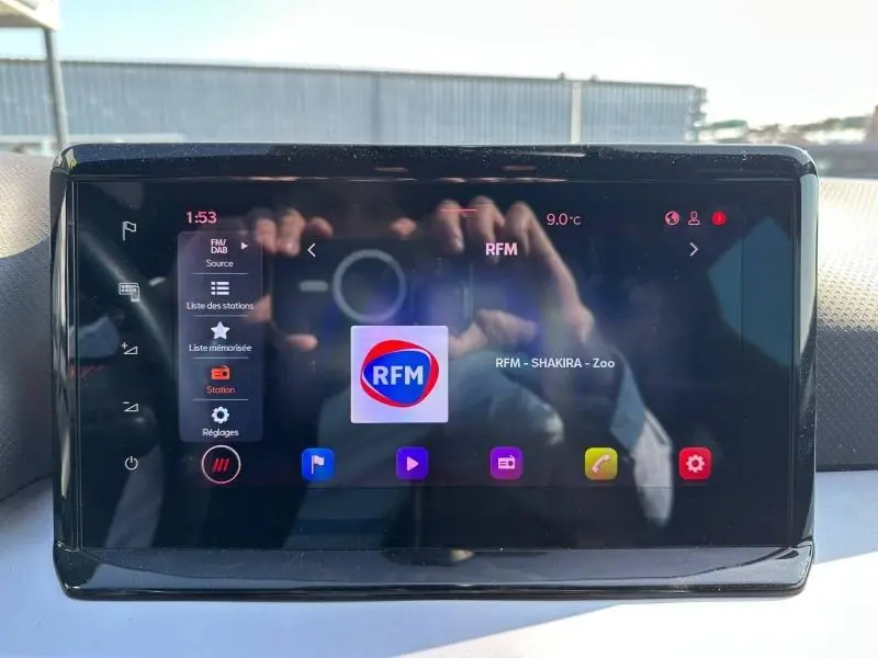 Écran tactile central du tableau de bord du SEAT Arona 2025 affichant la radio RFM, avec reflet des mains.