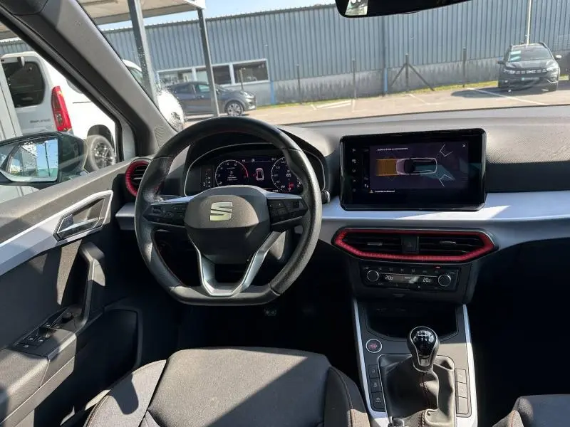Vue intérieure avant du SEAT Arona 2025 avec volant multifonction, écran tactile et détails rouges autour des aérateurs.