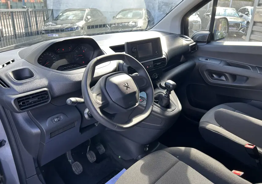 Vue intérieure côté conducteur du Peugeot Partner gris Artense 2025 avec tableau de bord et boîte manuelle visibles.