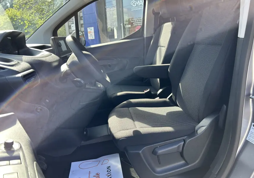 Vue intérieure côté conducteur du Peugeot Partner Dangel gris Artense, sièges tissu et tableau de bord simple avec écran central.
