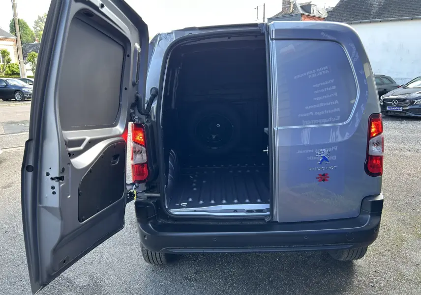 Vue arrière d'un Peugeot Partner gris Artense avec porte gauche ouverte et espace de chargement vide visible.