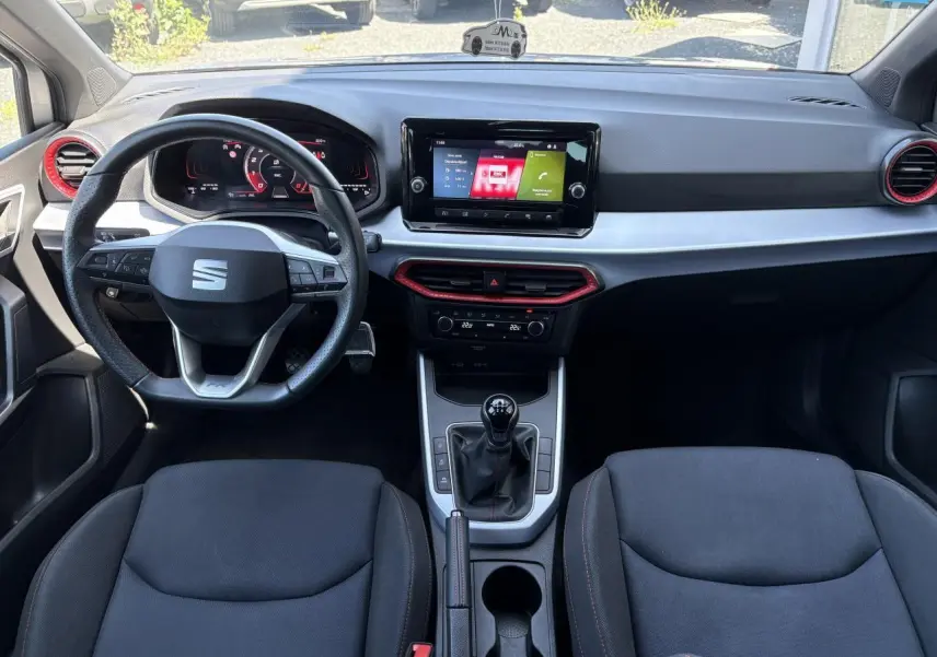 Vue intérieure avant du tableau de bord et volant cuir sport du SEAT ARONA 2024 avec inserts rouges et écran tactile central.